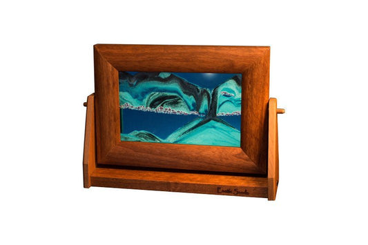 Moving sand art picture in alder wood frame with blue liquid sifting black/white sands on a swivel stand, made in USA by Exotic Sands.
